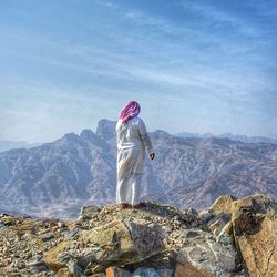 Rear view of man standing on mountain against sky