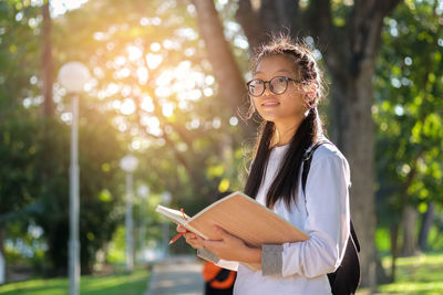 Portrait of woman standing by book against tree