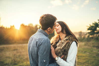 Young couple standing against sky during sunset