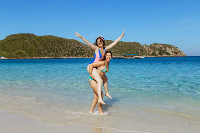 Woman carrying friend in sea against clear blue sky
