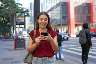 Brazilian girl using mobile phone with blurred background on paulista avenue in sao paulo, brazil