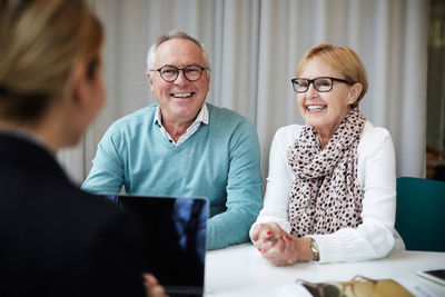 Smiling retired couple talking with female agent in real estate office