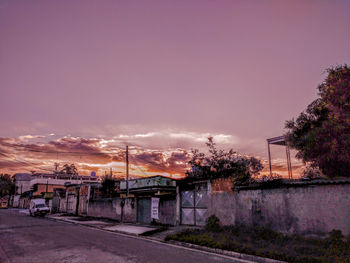 Street amidst trees against sky at sunset