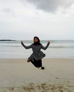 Full length of woman jumping at beach against sky