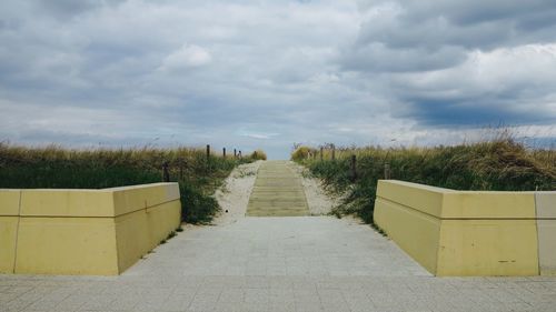 Footpath amidst grass against cloudy sky