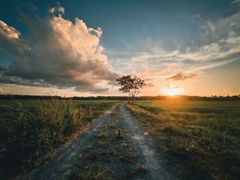 Road amidst field against sky during sunset