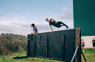 Friends jumping over wooden wall while exercising on land