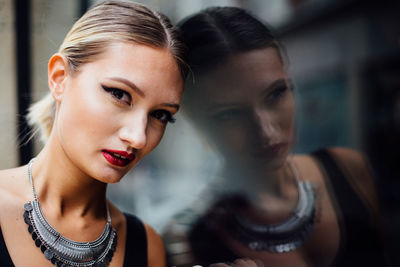 Close-up portrait of young woman by window in city