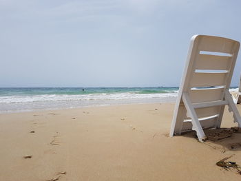 Deck chair on sand at beach against sky