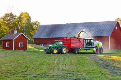 Tractor on field by houses against sky