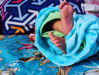 Low section of baby wrapped in blanket lying on bed at home