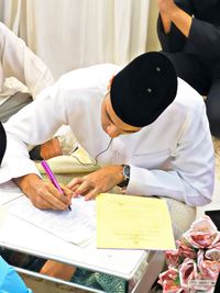 Man in traditional clothing signing in document at home