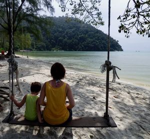 Rear view of boy sitting on shore against sky