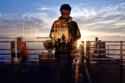 Reflection of man standing on railing by sea during sunset