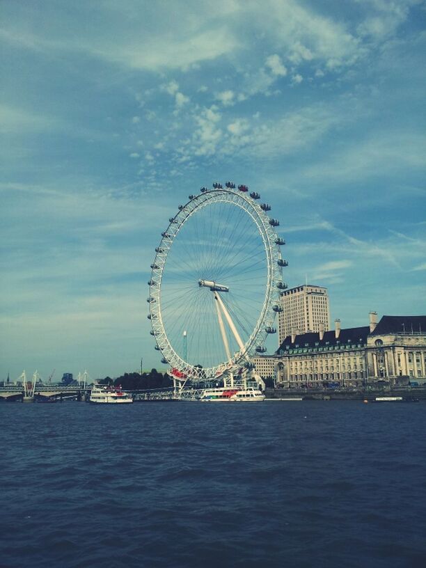 ferris wheel, waterfront, architecture, built structure, amusement park, water, sky, amusement park ride, arts culture and entertainment, nautical vessel, building exterior, tourism, travel destinations, sea, travel, cloud - sky, famous place, city, transportation, river