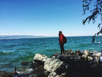 Woman standing on rock by sea against blue sky