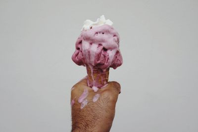 Cropped hand of man holding ice cream cone against white background