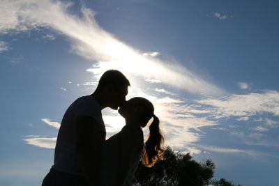 Low angle view of man and woman kissing against sky on sunny day