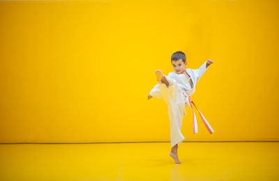 Portrait of cute boy practicing martial arts against yellow wall