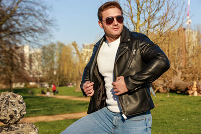 Young man wearing sunglasses and leather jacket in park