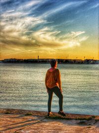 Rear view of man standing at beach against sky during sunset