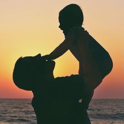 Silhouette mother carrying baby at beach against clear sky during sunset