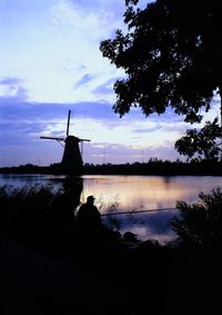 Silhouette of traditional windmill by lake against sky