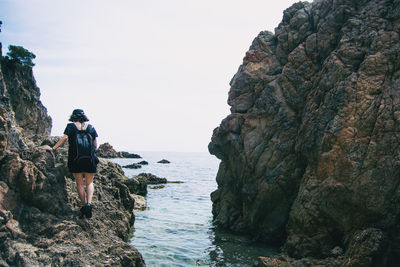 Rear view of man standing on rock by sea against sky