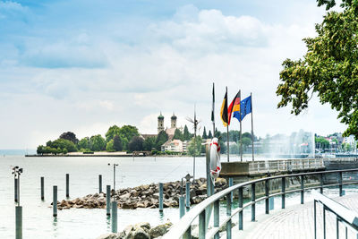 Flags on pier in sea against cloudy sky