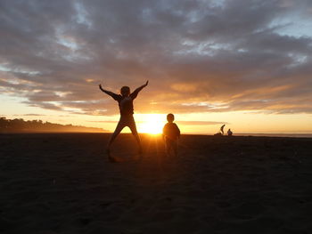 Silhouette siblings against sky during sunset