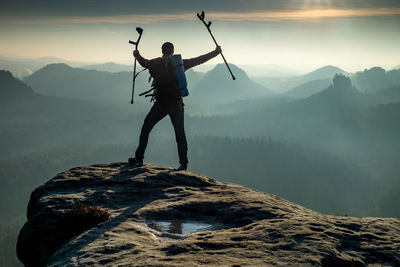 Happy man with arms outstretched holding crutches at mountain valley in sunset. personal motivation