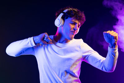 Young man with arms raised standing against black background