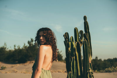 Young woman standing on cactus against sky