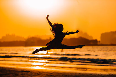 Silhouette man with arms raised in sea during sunset