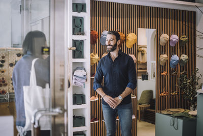 Smiling salesman looking at female customer arriving in clothing store