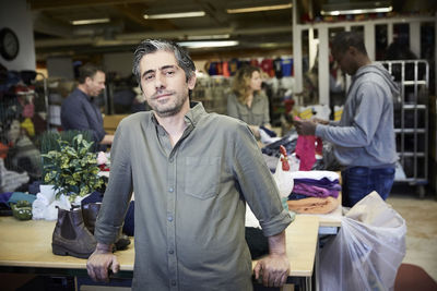 Portrait of confident mature man standing against colleagues working in warehouse