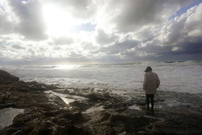 Man standing on rock against cloudy sky