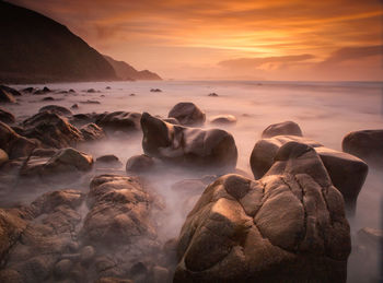 Rocks in sea against sunset sky