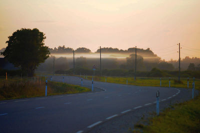 Road by trees on field against sky during sunset