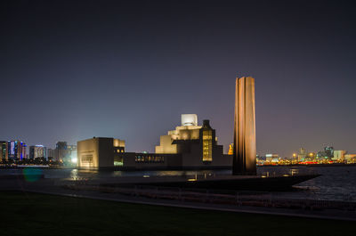 Museum of islamic art doha, qatar. illuminated buildings by river against sky in city at night