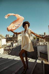 Full length of young woman standing against sky in city