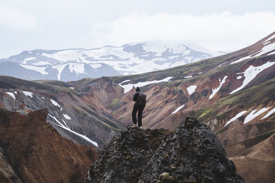 Rear view of man standing on rock against mountains during winter