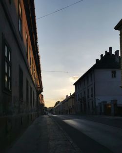 Empty road amidst buildings against sky at sunset