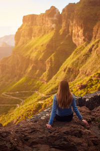 Rear view of woman sitting on rock