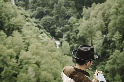 High angle view of man wearing hat while holding mobile phone on mountain against trees