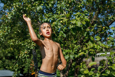 Shirtless boy standing against tree