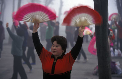 Mid adult woman holding hand fan while performing at park