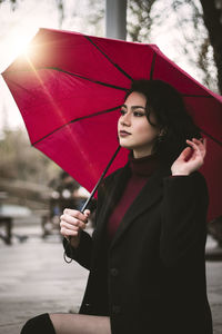 Woman looking away holding umbrella sitting in city