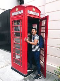 Full length portrait of happy young man standing on red phone