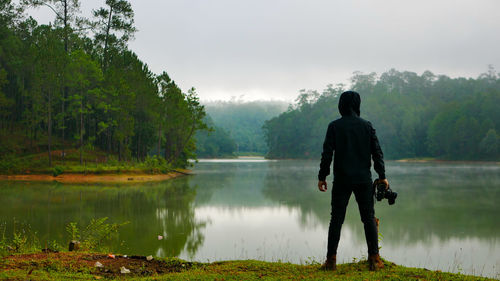 Rear view of man standing by lake against sky